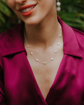 Primer plano de la modelo sonriendo que lleva un collar plateado con pequeñas estrellas distribuidas a lo largo de una cadena fina. Viste una blusa satinada de color fucsia y pendientes a juego con forma de estrella.