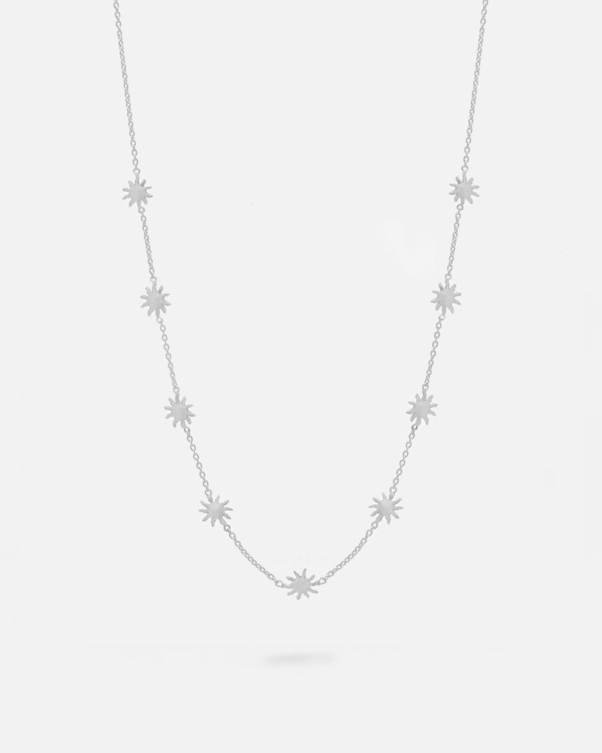 Collar plateado con pequeñas estrellas distribuidas de forma uniforme a lo largo de una cadena fina. Fondo liso y claro.