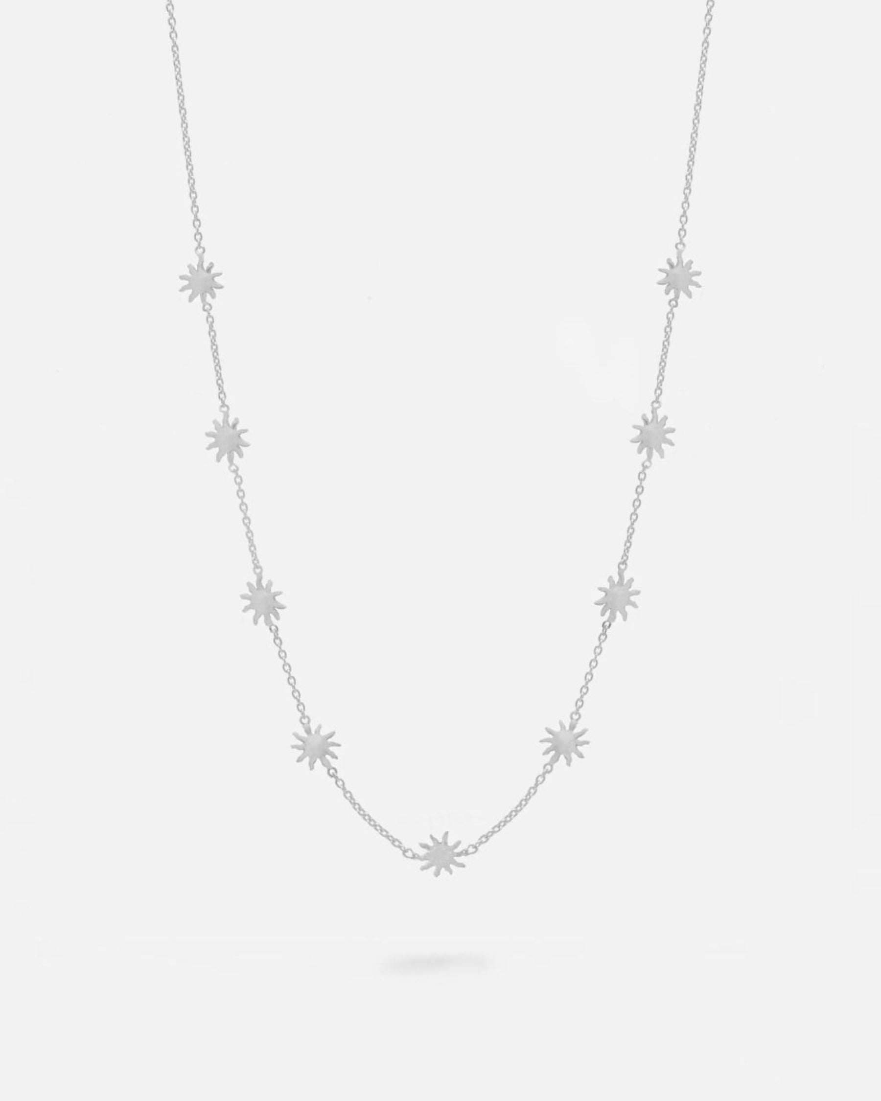 Collar plateado con pequeñas estrellas distribuidas de forma uniforme a lo largo de una cadena fina. Fondo liso y claro.