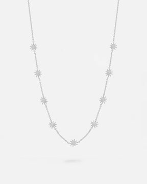 Collar plateado con pequeñas estrellas distribuidas de forma uniforme a lo largo de una cadena fina. Fondo liso y claro.