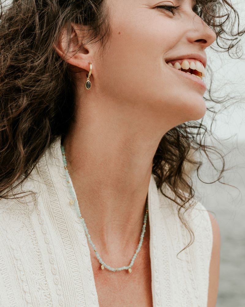 Modelo con conjunto de collar en piedra semipreciosa Aqua Calcedonia y aro dorado en piedra semipreciosa Jade de Isla Vurma