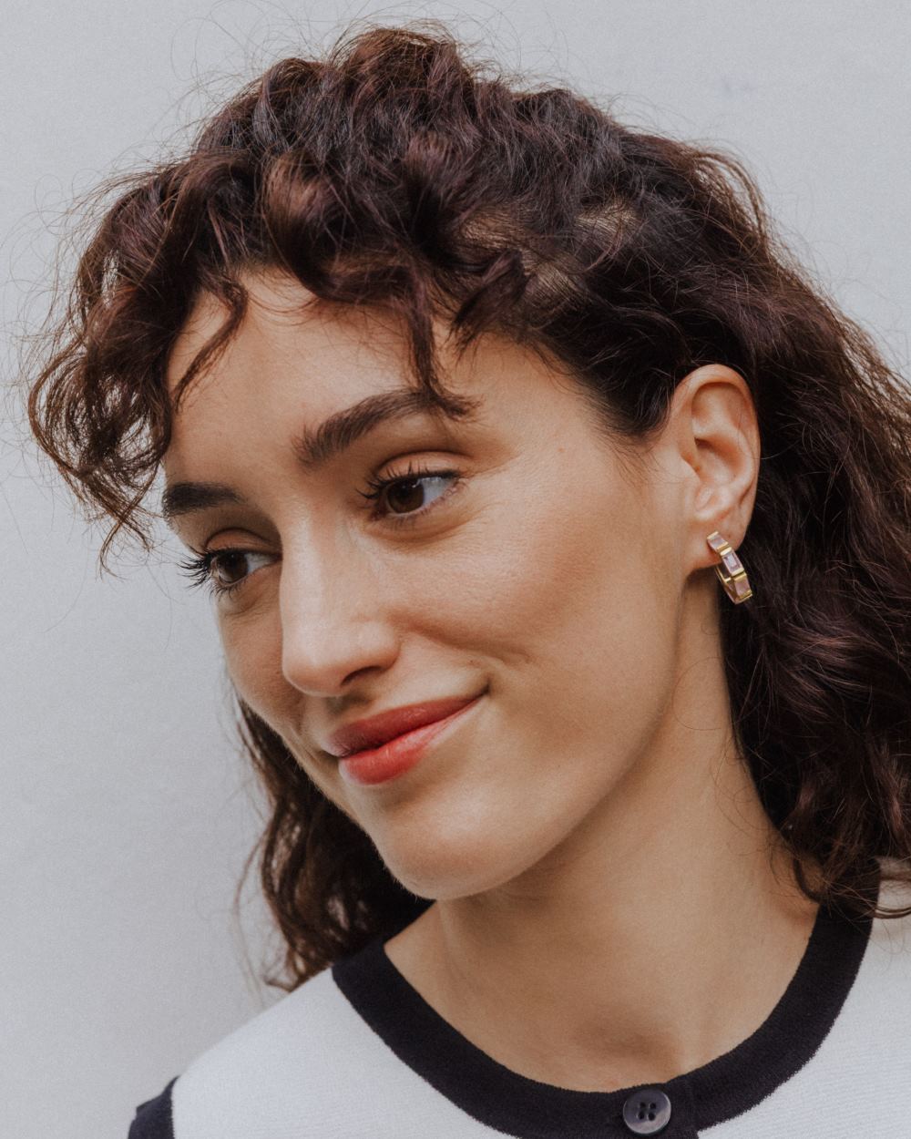 Pendiente de aro dorado con piedras semipreciosas rectangulares en Cuarzo Rosa, llevado por la modelo de cabello rizado y oscuro.