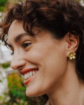 Pendiente dorado con forma de flor de cinco pétalos texturizados lucido en la oreja de la modelo.