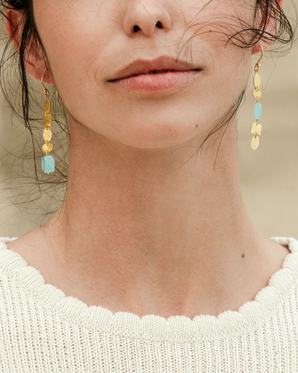 Pendientes dorados largos con forma orgánica y una piedra semipreciosa Aqua Calcedonia en el extremo de un pendiente y otra en medio del otro pendiente lucidos por la modelo