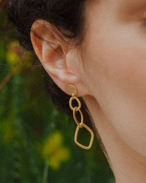 Primer plano de la modelo mirando hacia delante con los pendientes geométricos largos bañados en oro de 18 quilates de Isla Vurma