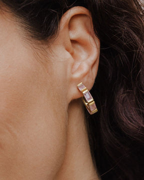 Pendiente de aro dorado con piedras semipreciosas rectangulares en cuarzo rosa, lucido en la oreja de la modelo. 