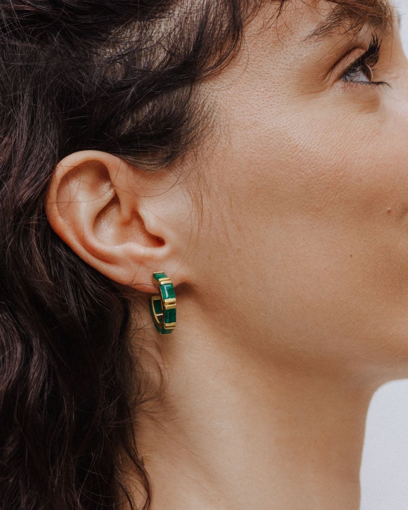 Pendiente de aro dorado con piedras semipreciosas rectangulares en Esmeralda, colocado en la oreja de una mujer de perfil.