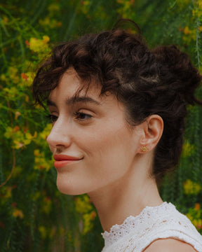 Modelo mirando a la izquierda y posando con los pendientes en forma de sol bañados en oro de 18k y cierre de tuerca tradicional de Isla Vurma