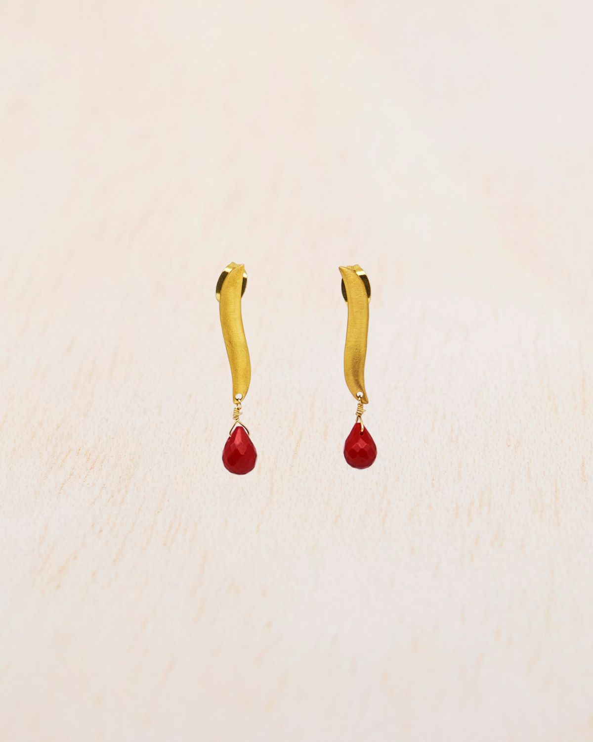 Primer plano de los pendientes bañados en oro de 18 quilates de alargada con piedra semipreciosa en Coral tallada en forma de lágrima