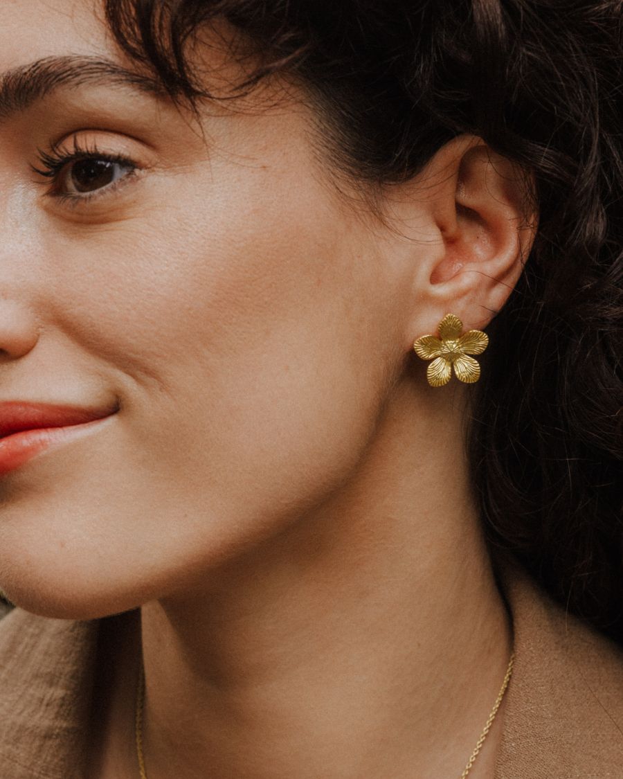 Pendiente dorado en forma de flor de cinco pétalos, con textura marcada.