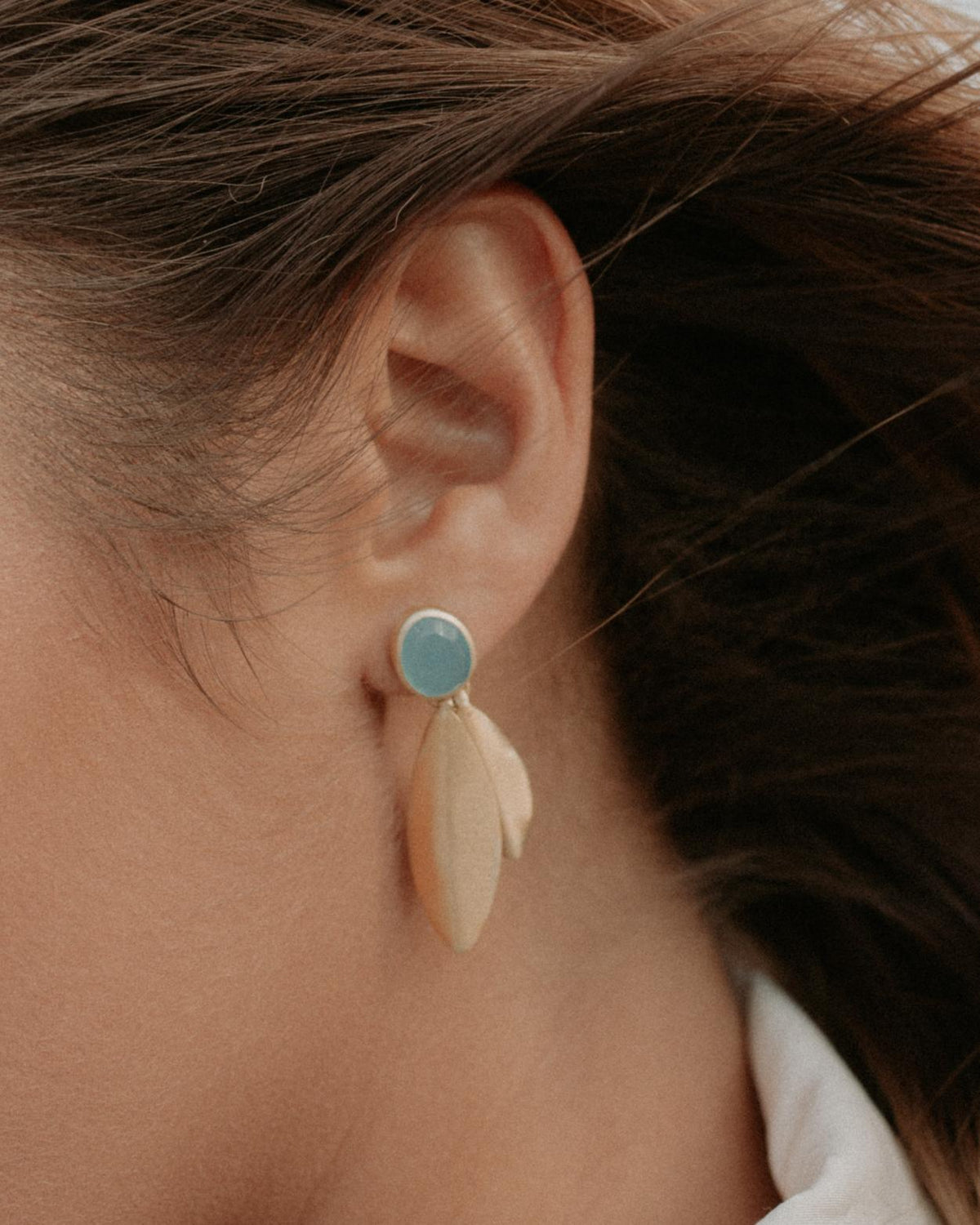Pendientes de latón bañado en oro con dos piezas alargadas en forma de hoja y piedra semipreciosa Aqua Calcedonia en el lóbulo de la oreja de una mujer