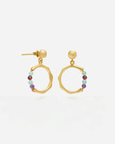 Primer plano de unos pendientes dorados con forma circular irregular y cierre de tuerca. En la parte inferior de cada aro cuelga una pequeña sección de cuentas redondas en piedras semipreciosas Amatista, Aqua Calcedonia, Aventurina Verde y Rubí. Fondo liso y claro.