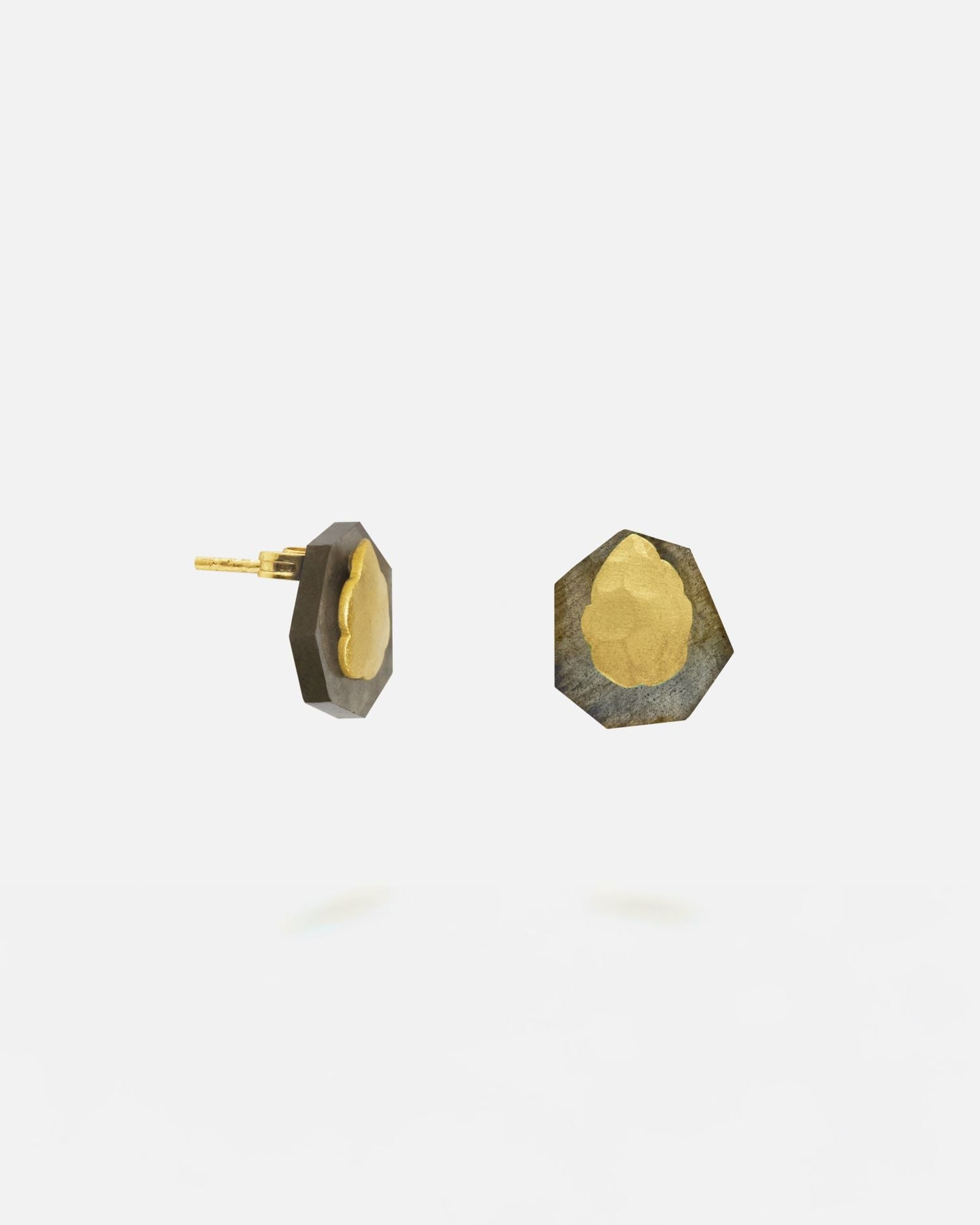 Pendiente pequeño con base irregular bañada en oro y piedra facetada de labradorita, colocado en el lóbulo de la oreja de una modelo con el cabello castaño suelto.