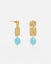 Pendientes dorados con dos piezas rectangulares texturizadas unidas en cascada y una cuenta ovalada azul turquesa colgante. Fondo blanco liso.