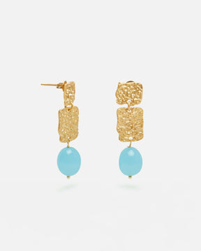 Pendientes dorados con dos piezas rectangulares texturizadas unidas en cascada y una cuenta ovalada azul turquesa colgante. Fondo blanco liso.