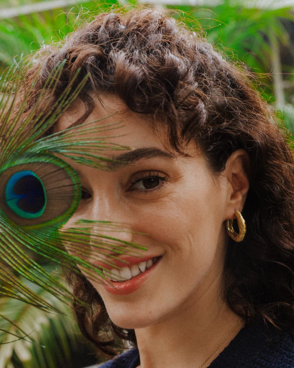 Primer plano de la modelo con pluma de pavo real llevando los pendientes gruesos circulares irregulares bañados en oro de 18k de Isla Vurma