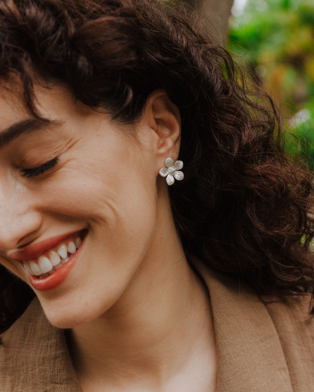 Pendientes plateados con forma de flor de cinco pétalos grabados, lucidos en la oreja de la modelo.