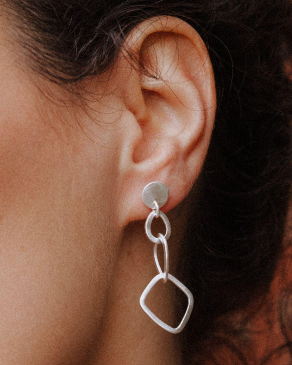 Primer plano de la modelo con los pendientes geométricos largos bañados en plata 925 de Isla Vurma