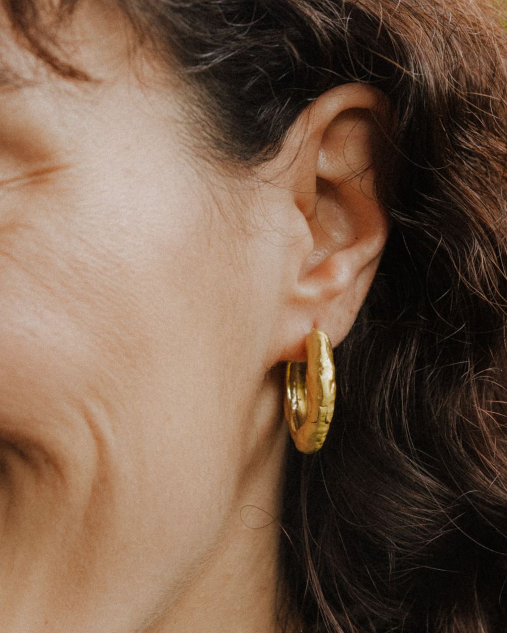Primer plano de la modelo llevando los pendientes gruesos irregulares circulares bañados en oro de 18k de Isla Vurma