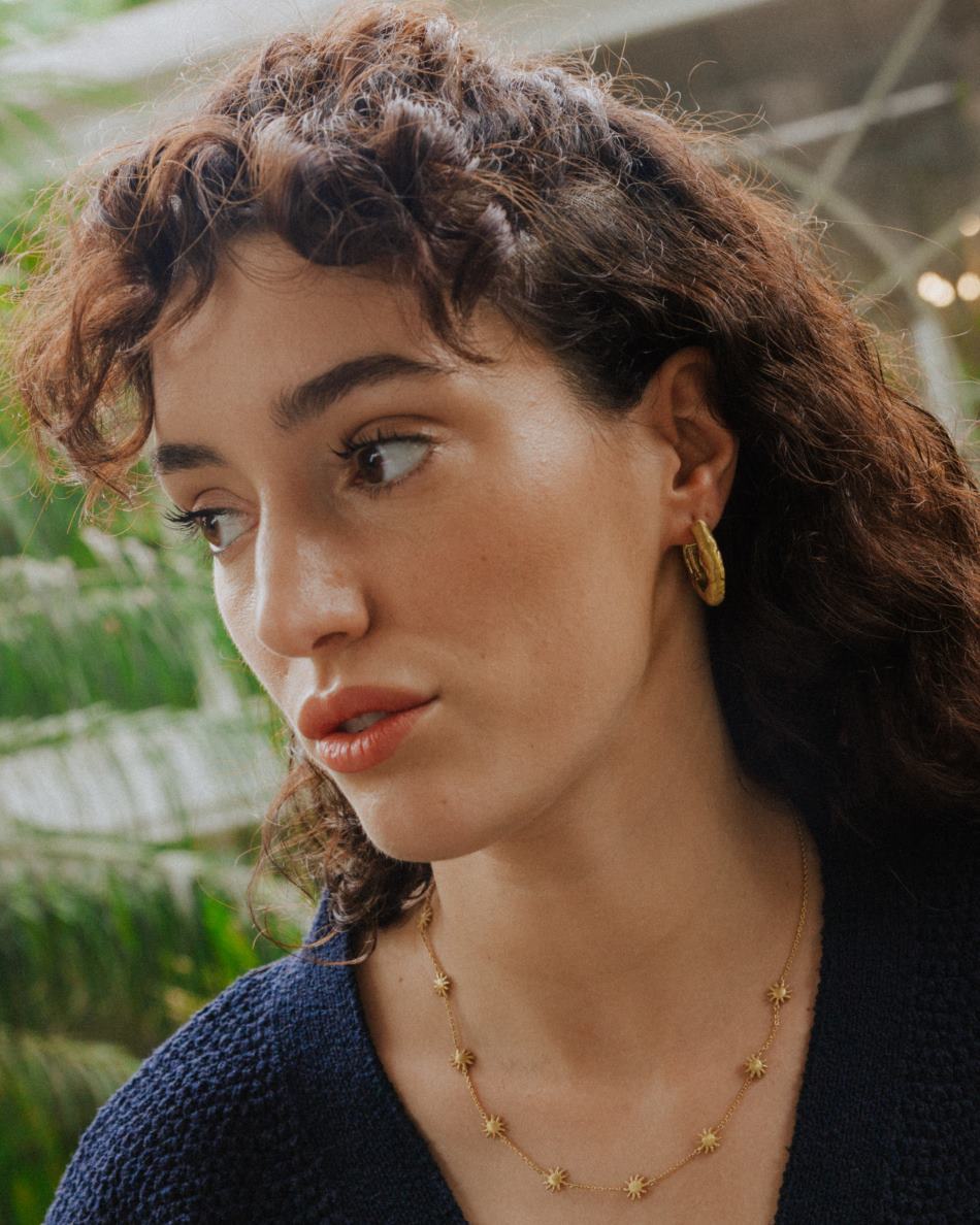 Modelo con conjunto bañado en oro de 18 quilates de pendientes circulares irregulares y collar con formas de girasol doradas de Isla Vurma