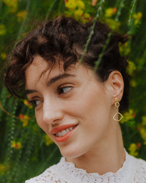 Primer plano de la modelo mirando hacia la izquierda sonriente con los pendientes geométricos largos bañados en oro de 18k de Isla Vurma