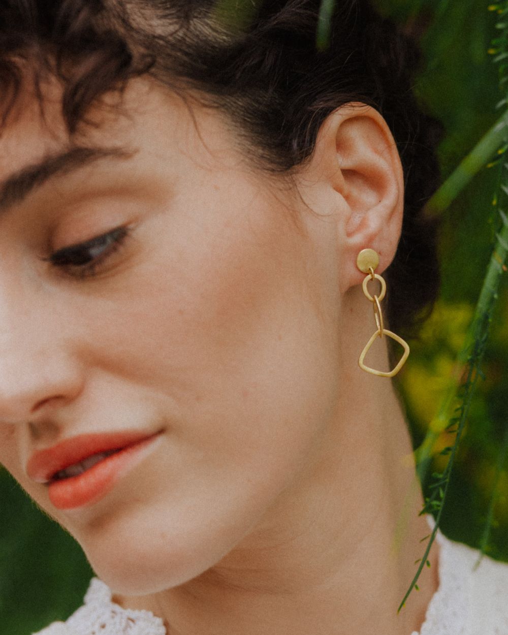 Primer plano de la modelo mirando hacia abajo con los pendientes geométricos largos bañados en oro de 18k de Isla Vurma