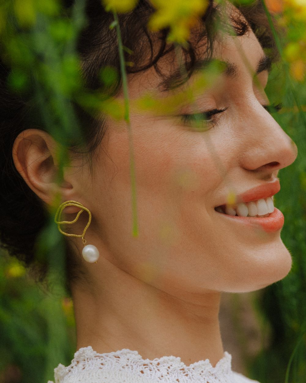 Modelo con fondo vegetal luciendo los pendientes bañados en oro de 18 quilates irregulares con Perla Natural en forma de mini aceituna 