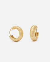 Par de aros dorados de grosor medio con textura martillada y cierre oculto, sobre fondo blanco.