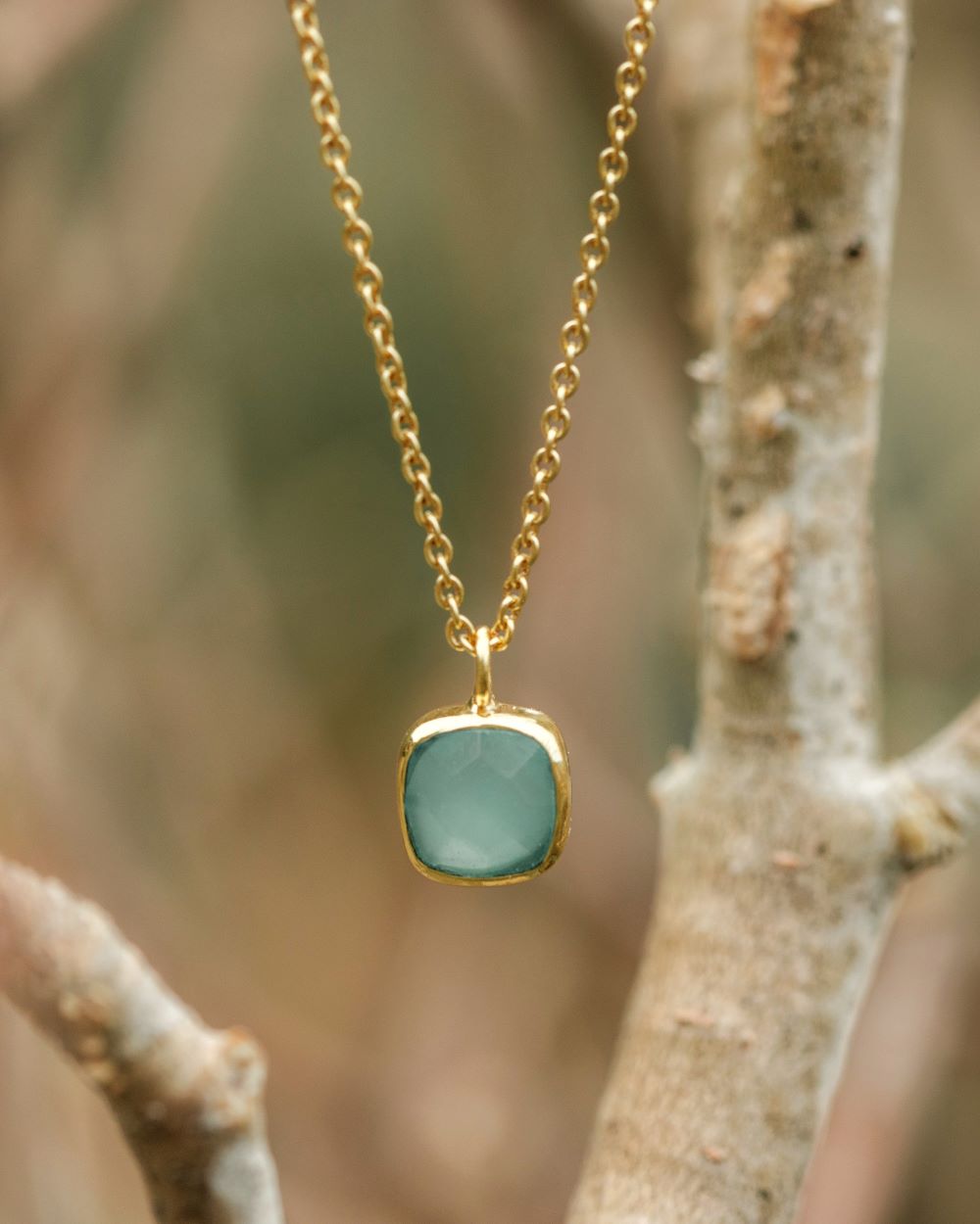 Primer plano del collar con pieza cuadrada disponible en Aqua Calcedonia, en un fondo natural de Isla Vurma