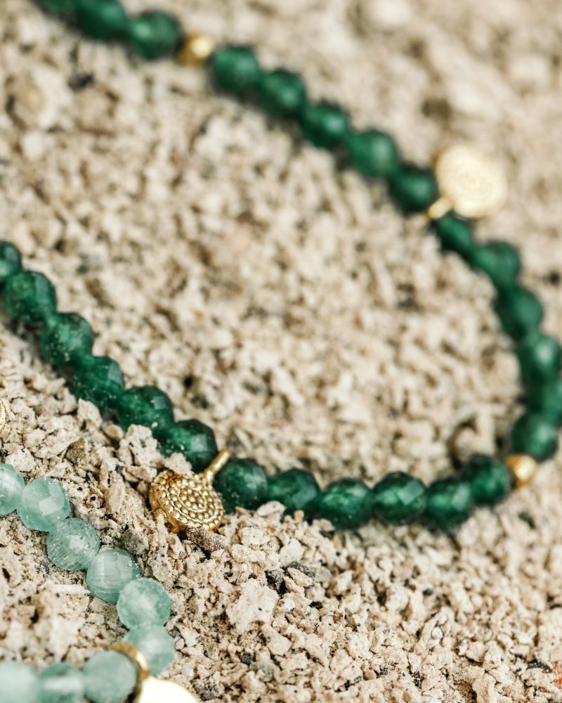 Collar con cuentas de Jade y pequeños discos dorados sobre fondo de piedra natural de Isla Vurma