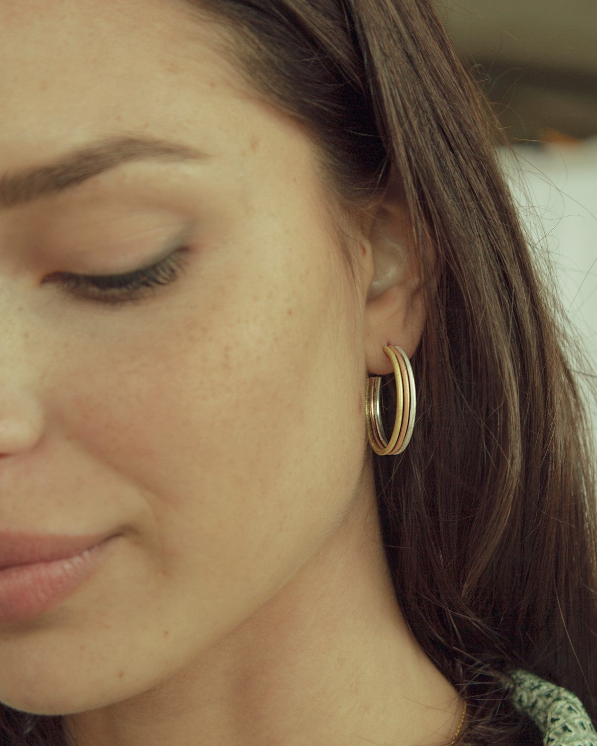 Modelo con pendientes de aro tricolor bañados en oro de 18k, oro rosa y plata 925, fondo natural y luz suave.