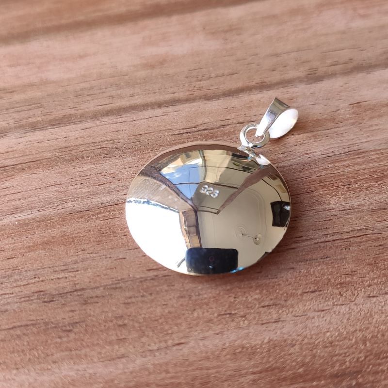 Primer plano del colgante que presenta una piedra de Santa Lucía enmarcada en un disco de textura cepillada con collar bañado en plata 925 visto de la parte de atrás en plateado brillante y con los números 925