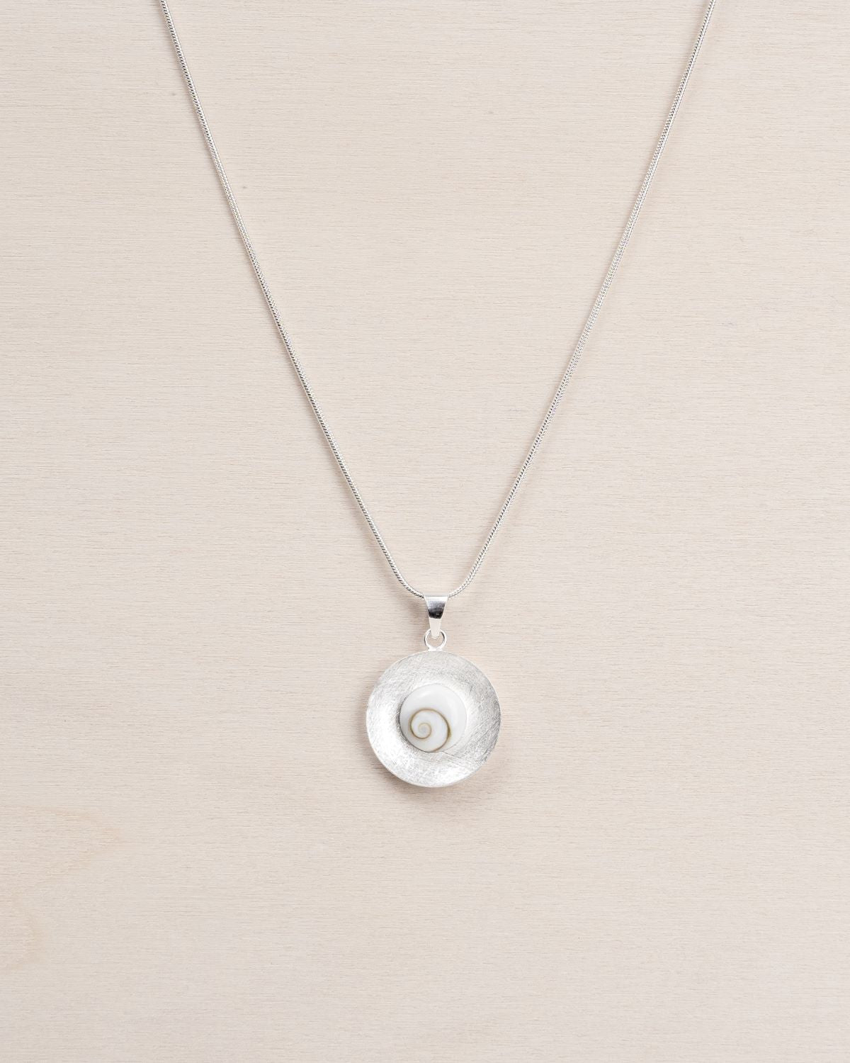 Primer plano del colgante que presenta una piedra de Santa Lucía enmarcada en un disco de textura cepillada con collar bañado en plata 925