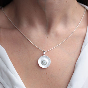 Primer plano del cuello de la modelo luciendo el colgante que presenta una piedra de Santa Lucía enmarcada en un disco de textura cepillada con collar bañado en plata 925