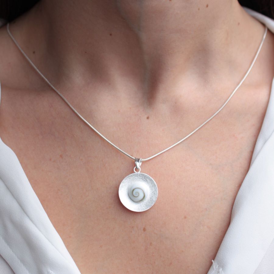 Primer plano del cuello de la modelo luciendo el colgante que presenta una piedra de Santa Lucía enmarcada en un disco de textura cepillada con collar bañado en plata 925