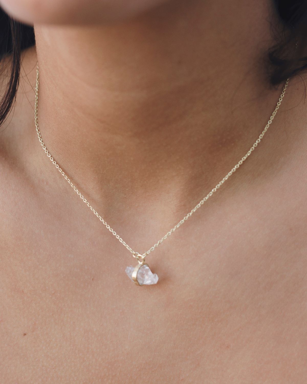 Modelo en primer plano con collar bañado en oro de 18 quilates, con piedra semipreciosa Piedra de Luna, sujetada por una pequeña pieza rectangular dorada de Isla Vurma