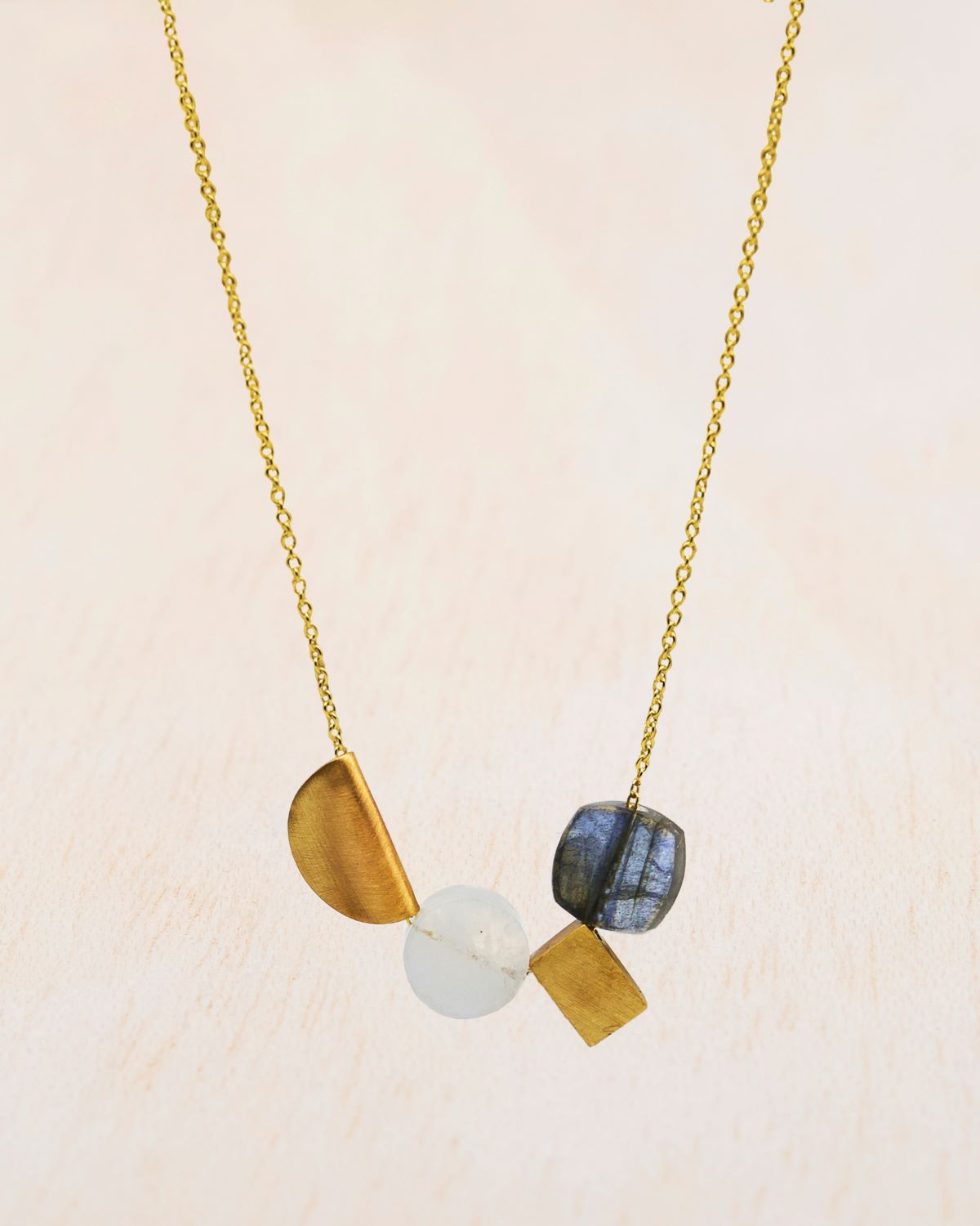 Primer plano del collar bañado en oro de 18k con piedra Labradorita y Piedra de Luna junto a dos piezas geométricas en oro de Isla Vurma
