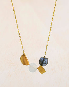 Primer plano del collar bañado en oro de 18k con piedra Labradorita y Piedra de Luna junto a dos piezas geométricas en oro de Isla Vurma