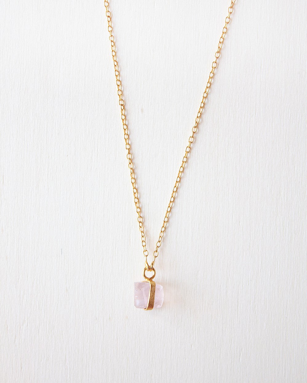 Primer plano del collar bañado en oro de 18 quilates con piedra semipreciosa de Cuarzo Rosa sujeta por una pequeña pieza dorada de Isla Vurma