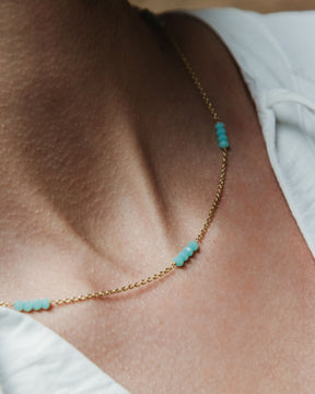 Modelo con camiseta blanca y collar bañado en oro de 18 quilates compuesto por pequeñas tiras de piedras semipreciosas Aqua Calcedonia de Isla Vurma