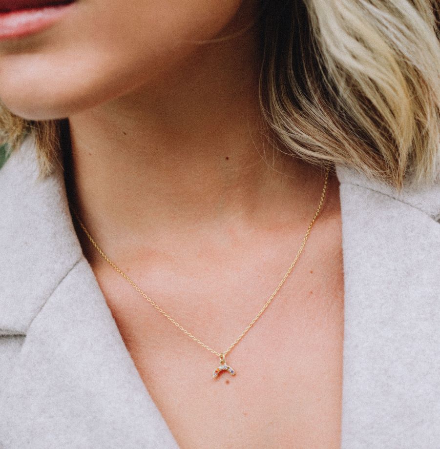 Modelo con collar dorado y una pequeña forma de arcoiris con piedras semipreciosas incrutadas de Isla Vurma