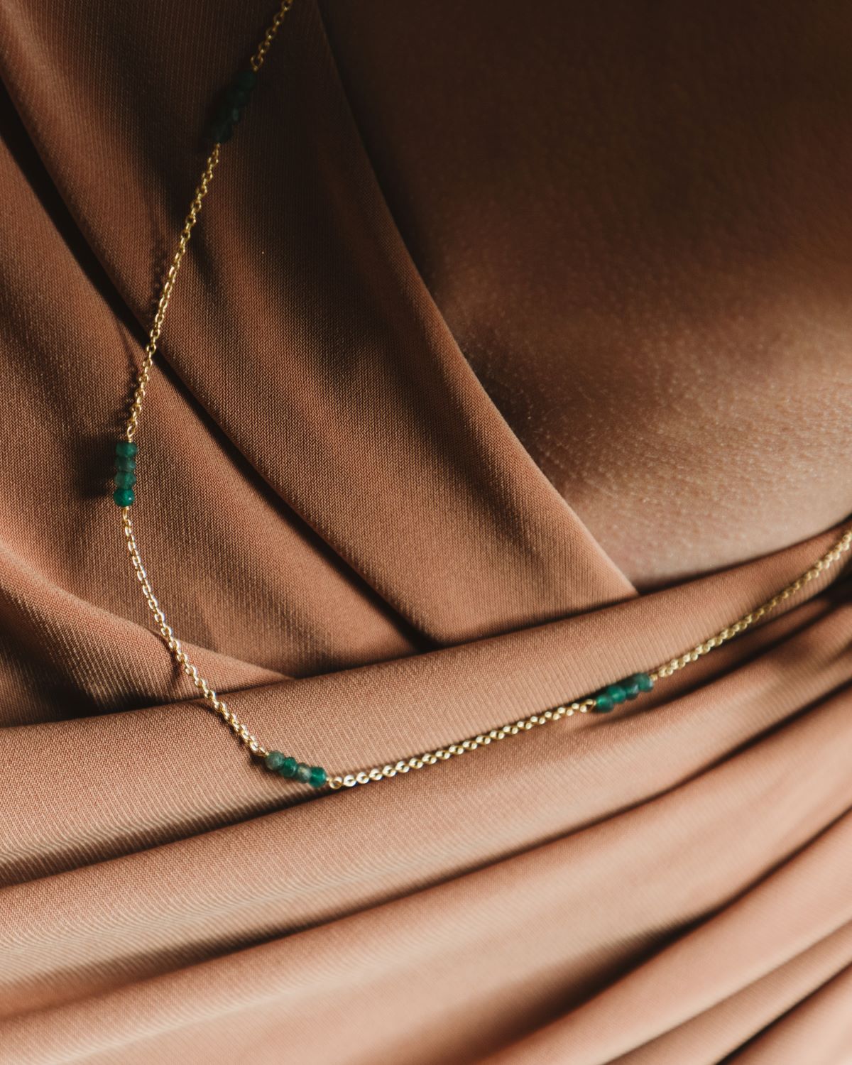 Modelo con camiseta marrón y collar bañado en oro de 18 quilates compuesto por pequeñas tiras de piedras semipreciosas Jade de Isla Vurma