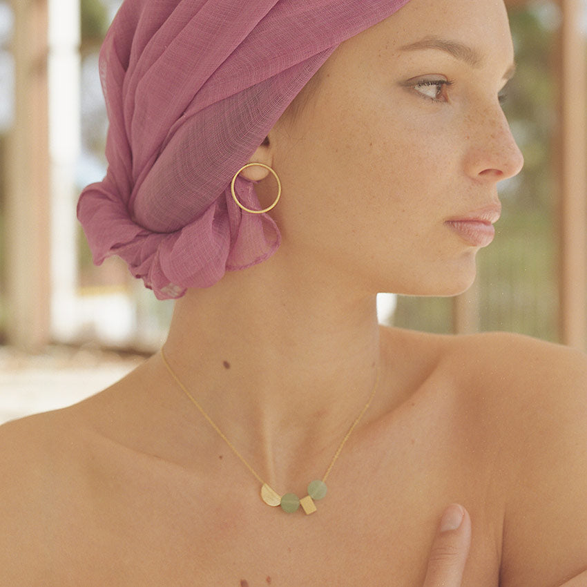 Modelo con conjunto de aro circular bañado en Oro y colgante con pieza circular y rectangular doradas y dos piedras semipreciosas en Aventurina Verde de Isla Vurma