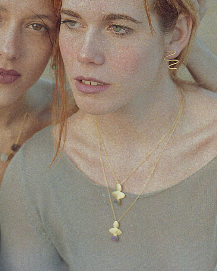 Dos modelos en primer plano con tres collares geométricos de piedras semipreciosas Aqua Calcedonia, Amatista y Moonstone, y pendientes bañados en Oro de 18k de Isla Vurma