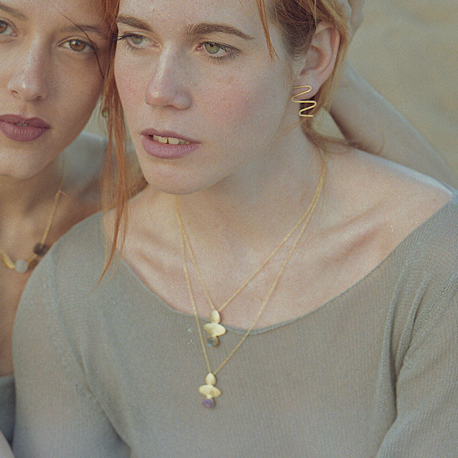 Dos modelos en primer plano con tres collares geométricos de piedras semipreciosas Aqua Calcedonia, Amatista y Moonstone, y pendientes bañados en Oro de 18k de Isla Vurma