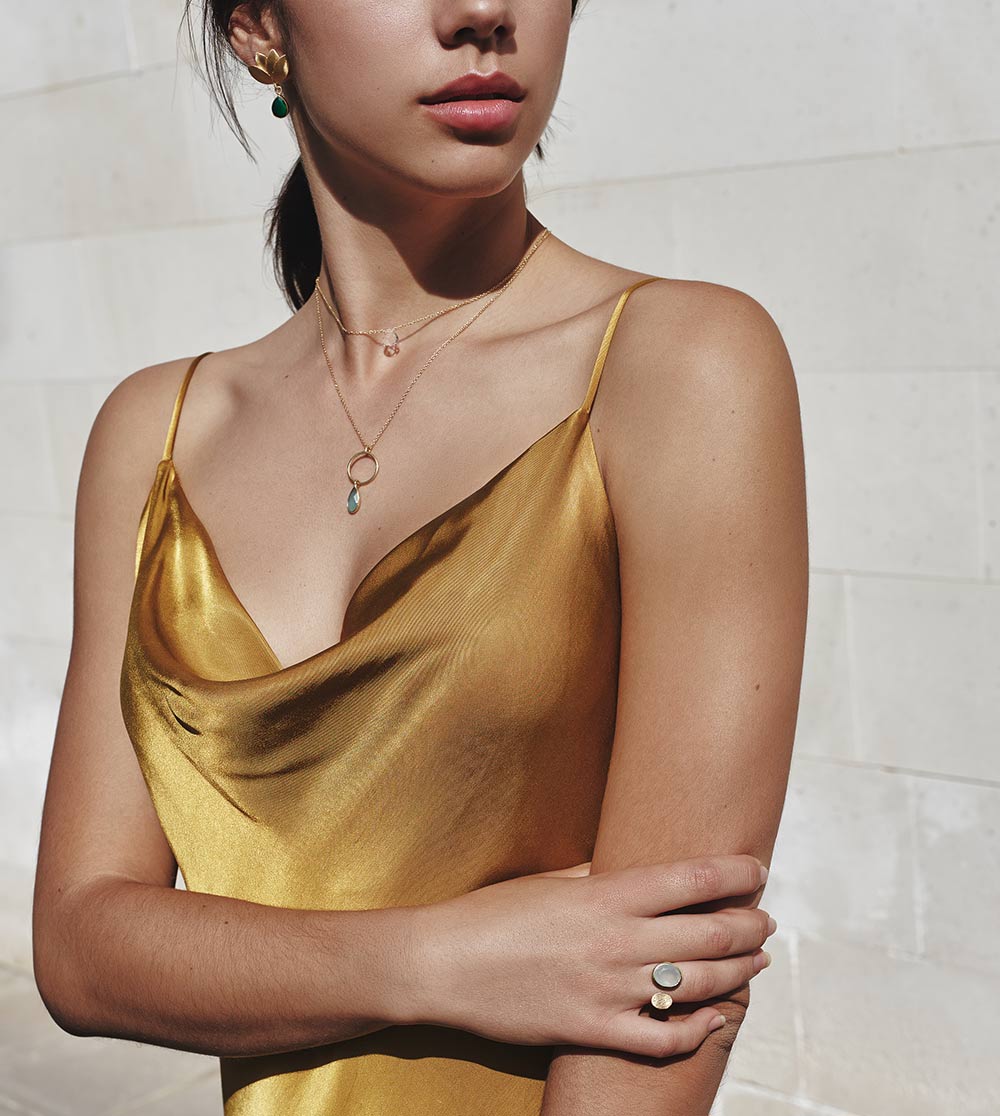 Modelo con pendientes bañados en oro y con piedra semipreciosa jade, collares con piedras semipreciosas Moonstone, Aqua Calcedonia y anillo con Piedra de Luna de Isla Vurma