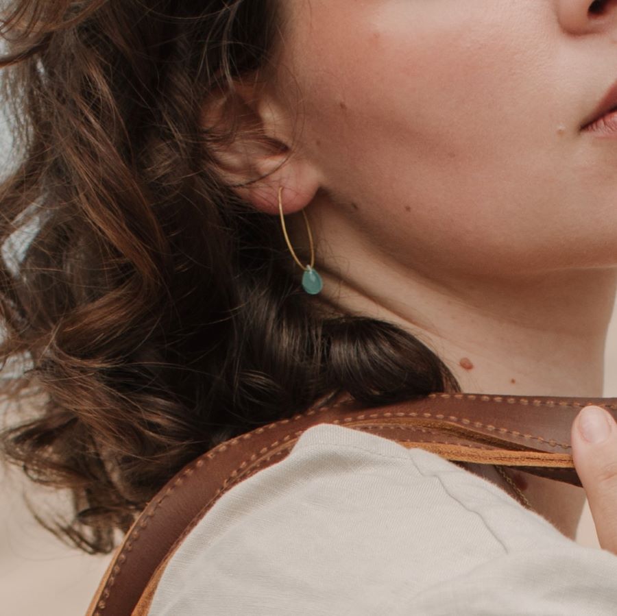 Primer plano de la oreja de la modelo luciendo los pendientes bañados en Oro de 18 quilates con piedra semipreciosa Aqua Calcedonia en forma de gota