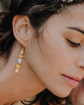 Pendiente dorado con piezas geométricas irregulares y una piedra semipreciosa Piedra Luna que aporta luminosidad al rostro de la modelo