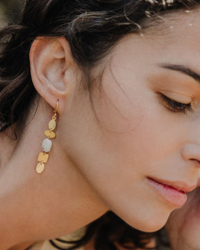 Pendiente dorado con piezas geométricas irregulares y una piedra semipreciosa Piedra Luna que aporta luminosidad al rostro de la modelo