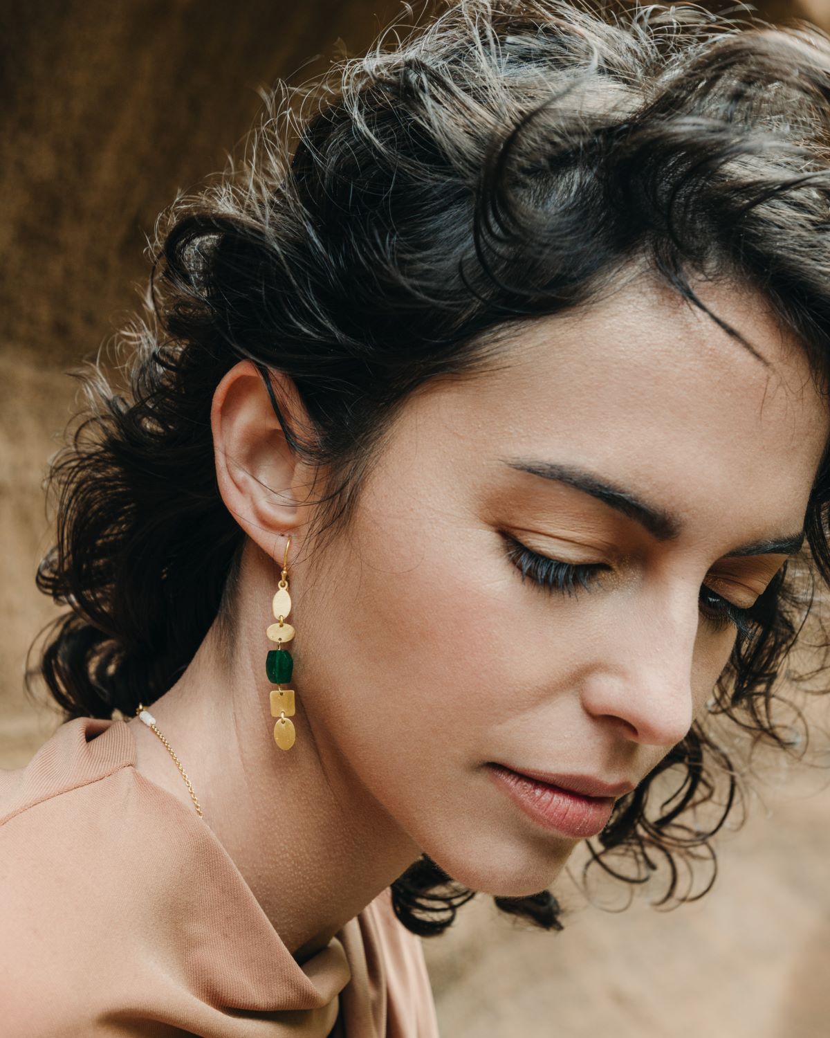 Primer plano de la modelo luciendo el pendiente dorado con formas geométricas orgánicas y una piedra semipreciosa Jade en el centro